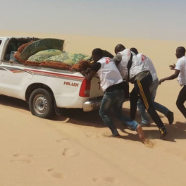 4 Mitarbeiter schieben ein Fahrzeug von Ärzte ohne Grenzen in einer Wüstenlandschaft.